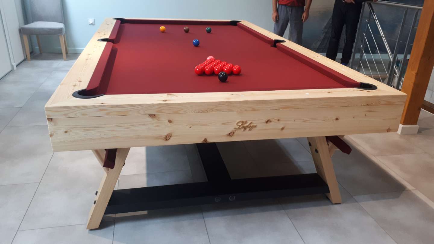 Billard classique décoré en bois naturel avec tirants et feutre rouge, posé sur un socle élégant dans une pièce intérieure. Billard classique décoration intérieure.