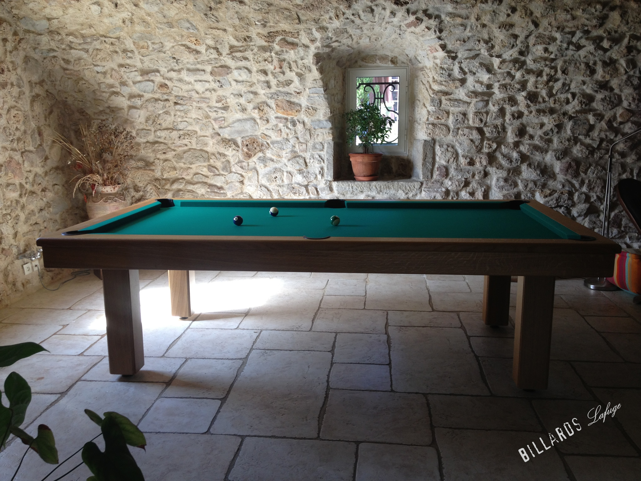 Table de billard avec plateau vert dans une pièce en pierre, vue d’ensemble sobre et lumineuse.