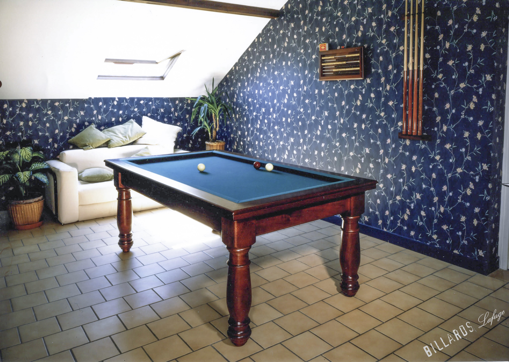 Un billard à tapis bleu et trois billes se trouve au centre d’une pièce.