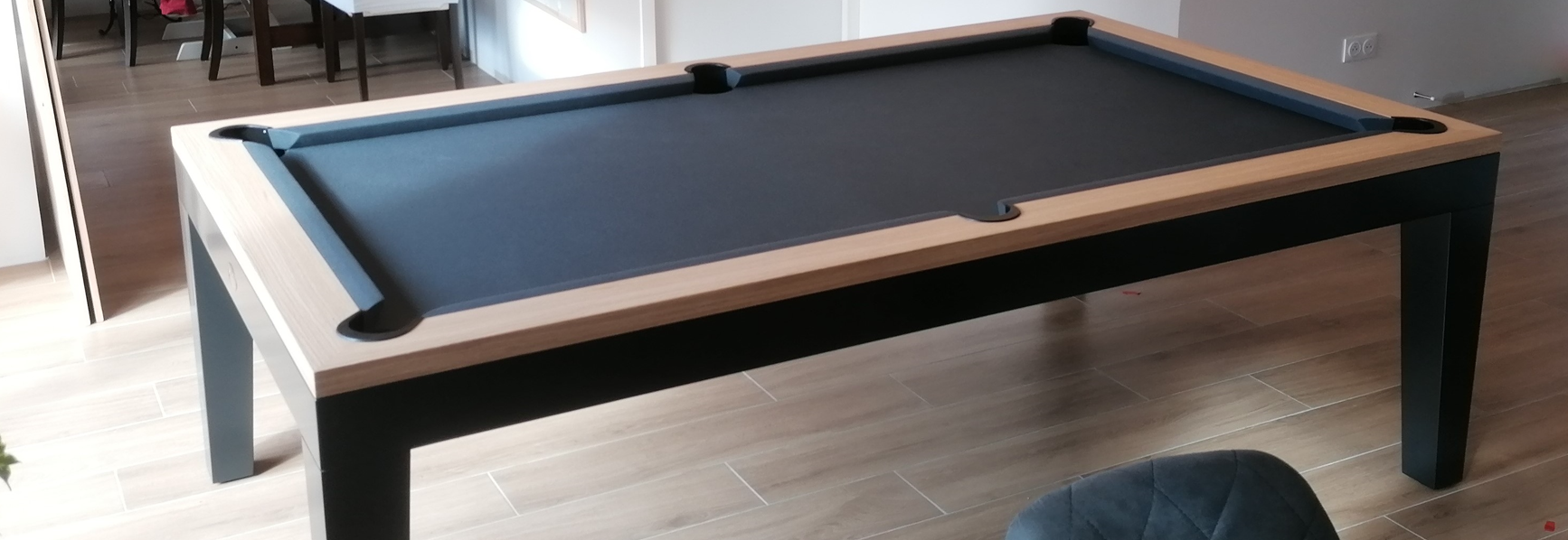 Table de billard à poser sur table avec plateau noir et cadre en bois clair dans une pièce.