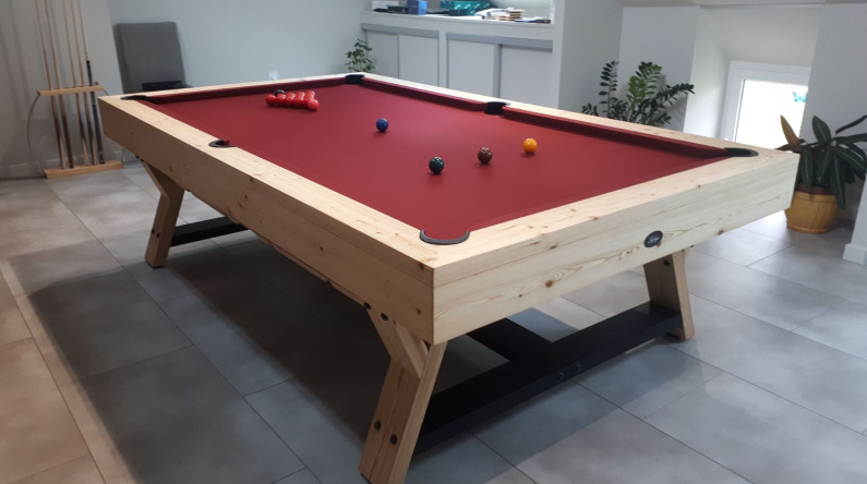 Table de billard en bois clair avec tapis rouge dans une pièce moderne.