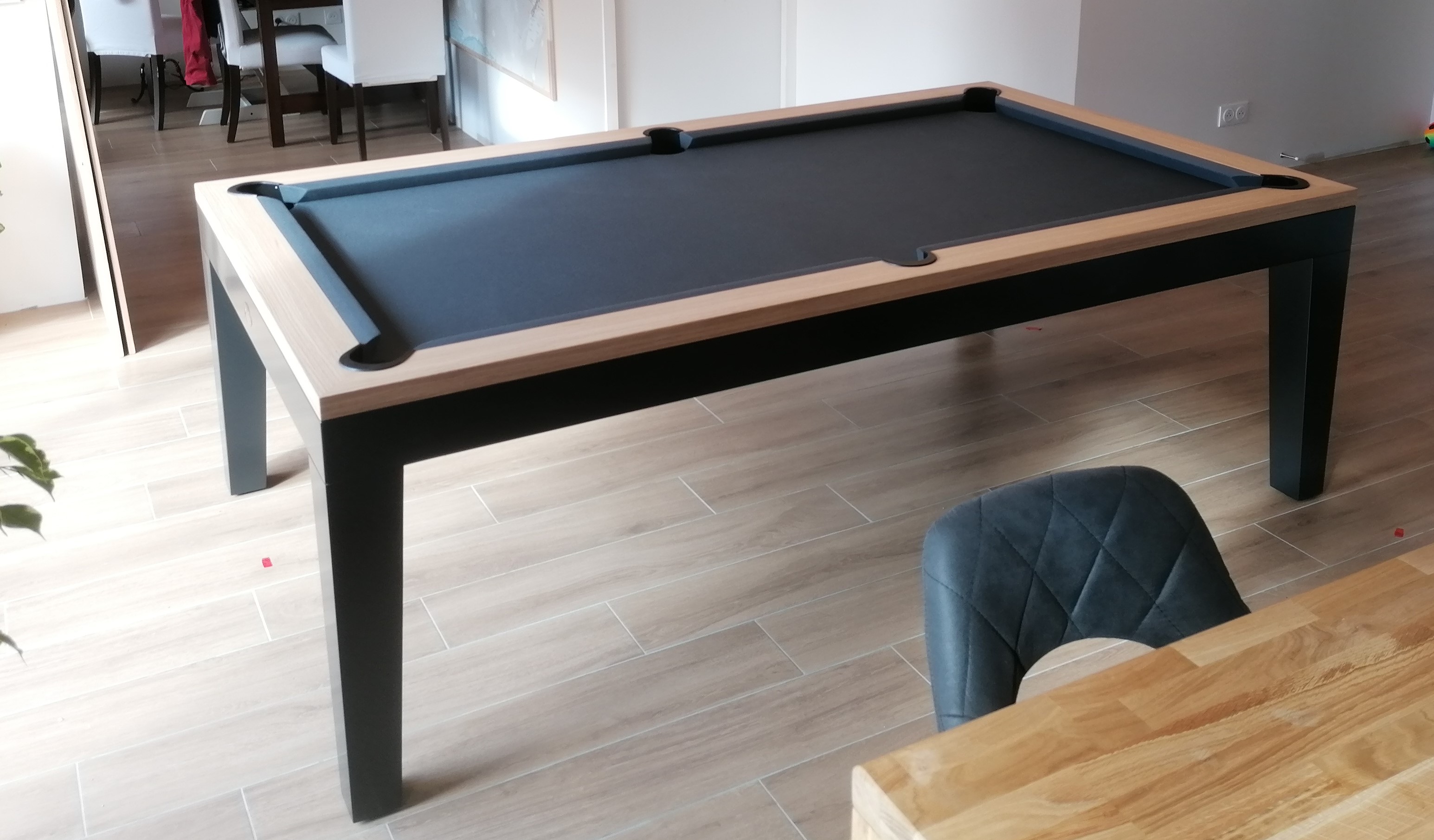 Table de billard moderne avec table noire et rebord clair sur plancher en bois.