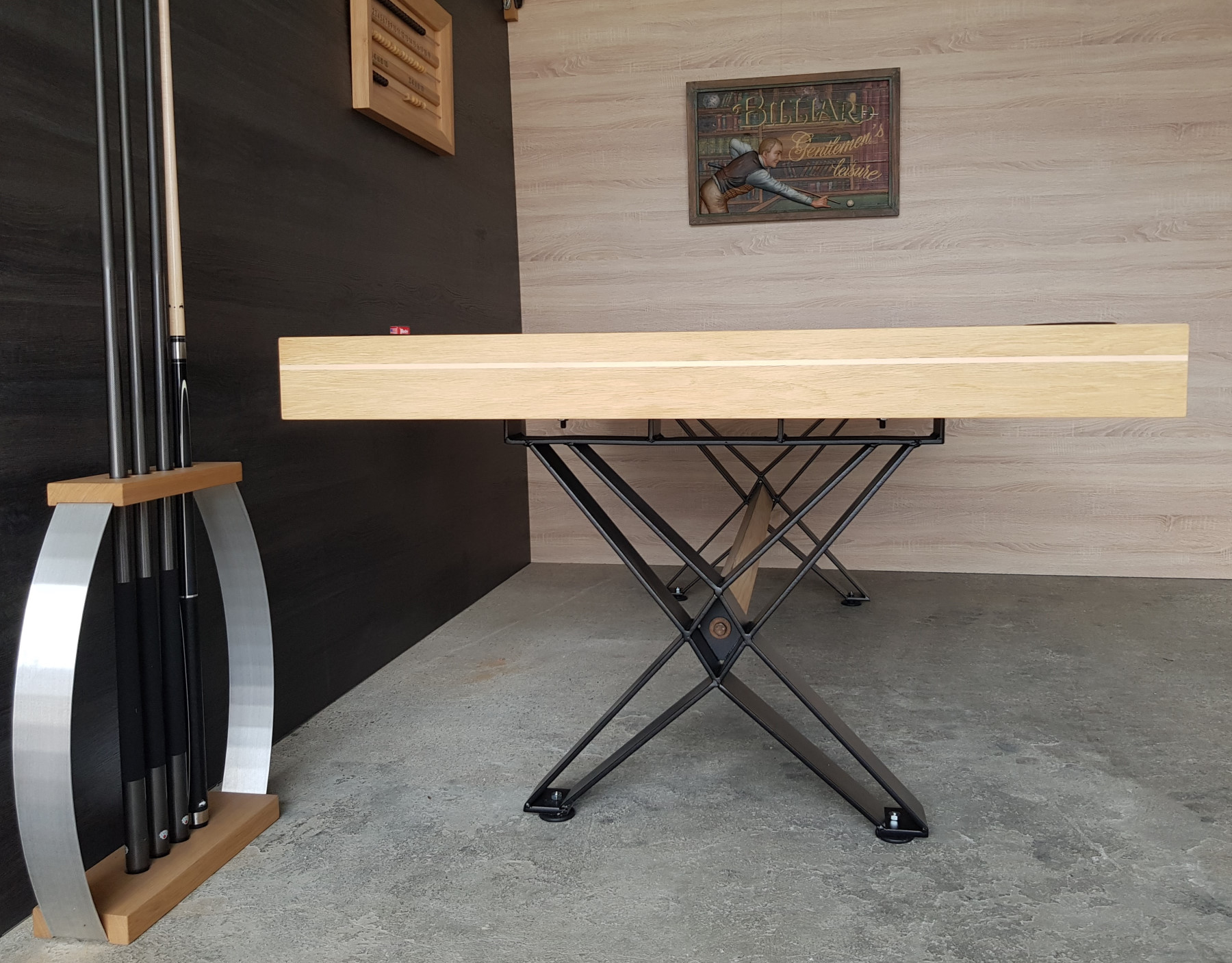 Table de billard vue de côté avec cadre métallique noir et pieds en X sur sol en béton, ardoises murales et décoration au